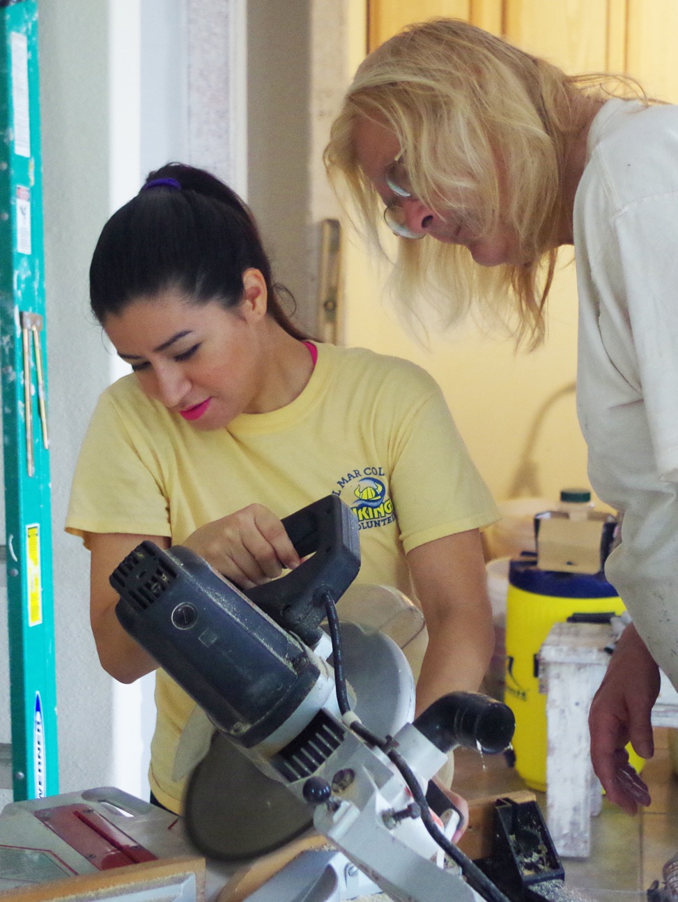 Erica Funes (left) gets help from Mari Randolph on how to properly use a miter saw on door trim pieces while helping build a Habitat for Humanity house.